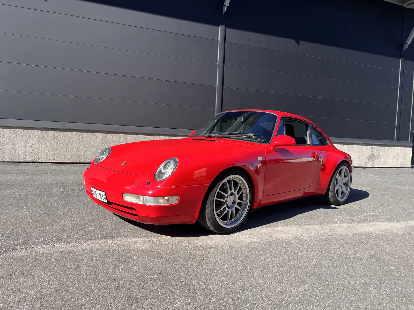 Röd Porsche fotograferad i solljus utanför verkstaden.