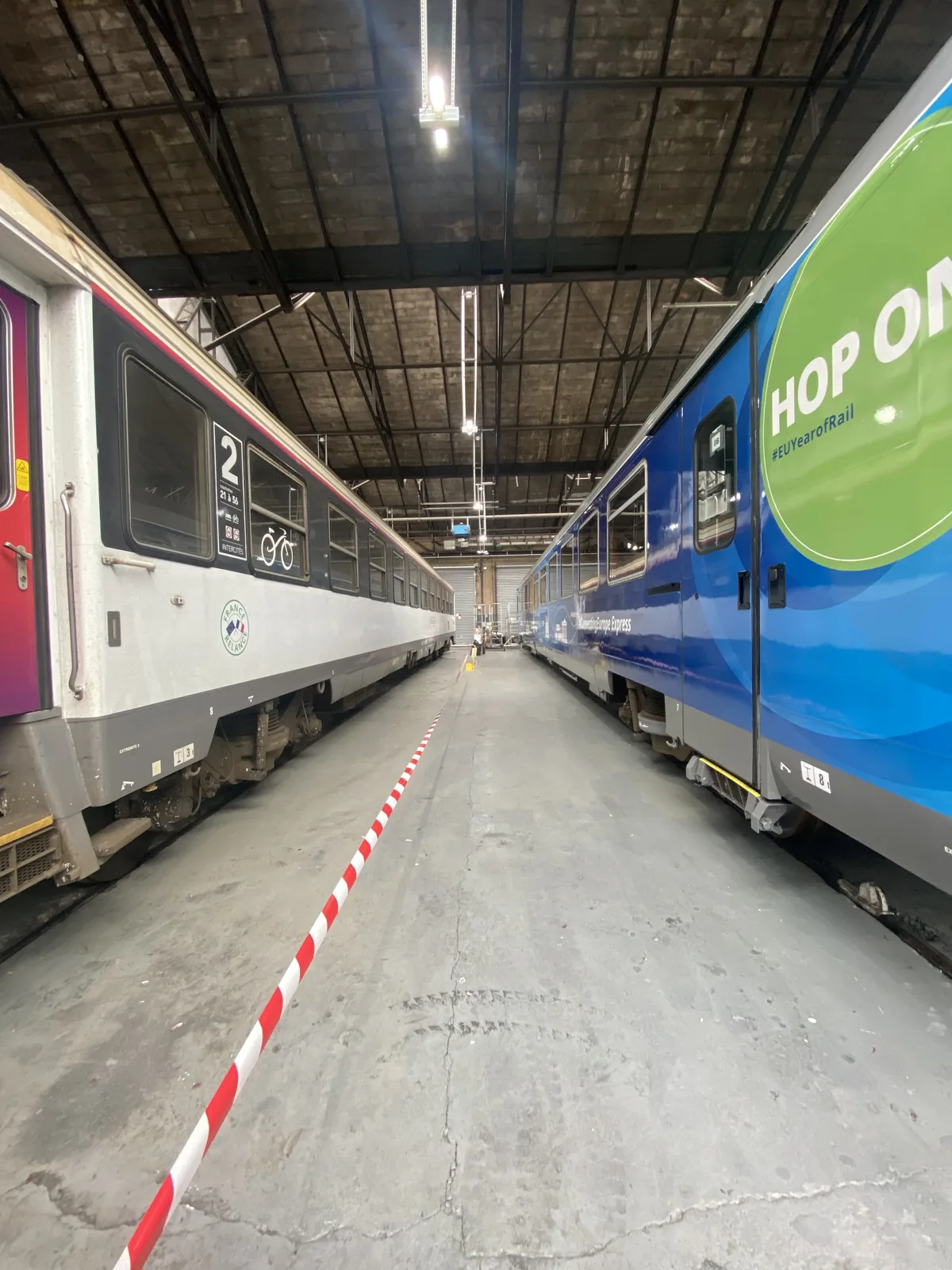 Blå kampanjdekor längs en tågvagn i verkstadsmiljö.